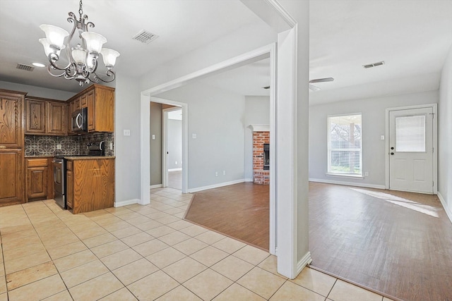 kitchen featuring a brick fireplace, light tile patterned floors, stainless steel appliances, ceiling fan with notable chandelier, and decorative backsplash