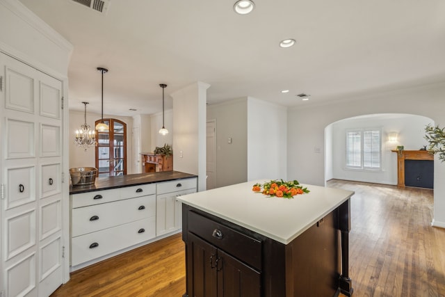 kitchen with white cabinetry, crown molding, wood-type flooring, a center island, and hanging light fixtures