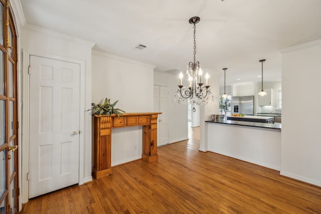 kitchen with hardwood / wood-style flooring, ornamental molding, stainless steel fridge, and a chandelier