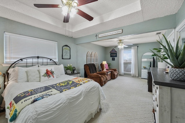 carpeted bedroom featuring ceiling fan, a tray ceiling, and a textured ceiling