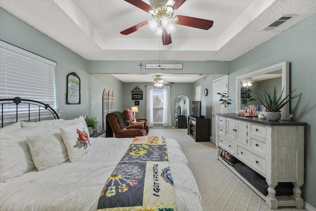 bedroom featuring light colored carpet, a textured ceiling, and a tray ceiling