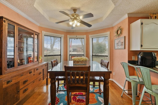 dining room with a textured ceiling, light hardwood / wood-style flooring, a raised ceiling, and ceiling fan