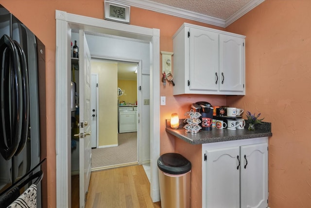 kitchen featuring black refrigerator, stacked washer and clothes dryer, crown molding, and white cabinets