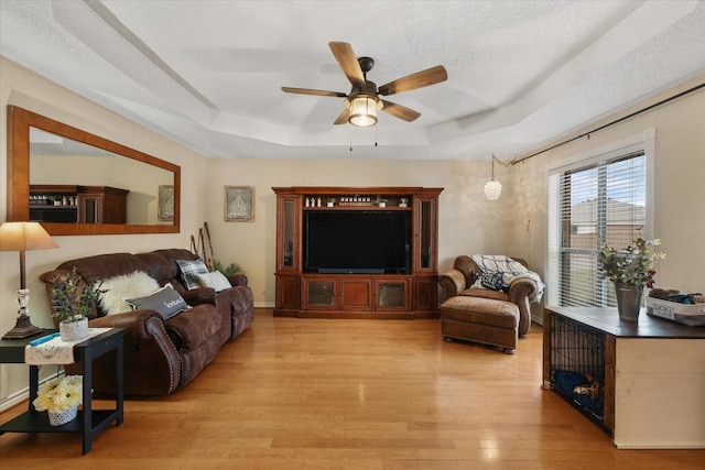 living room featuring ceiling fan, a textured ceiling, light hardwood / wood-style floors, and a tray ceiling