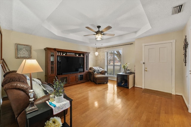 living room featuring ceiling fan, a textured ceiling, light wood-type flooring, and a tray ceiling