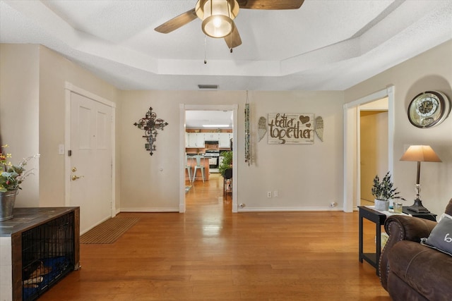 interior space with ceiling fan, light hardwood / wood-style floors, a raised ceiling, and a textured ceiling