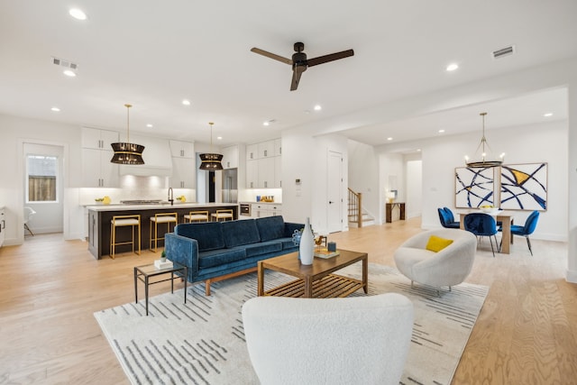 living room with sink, ceiling fan with notable chandelier, and light hardwood / wood-style flooring