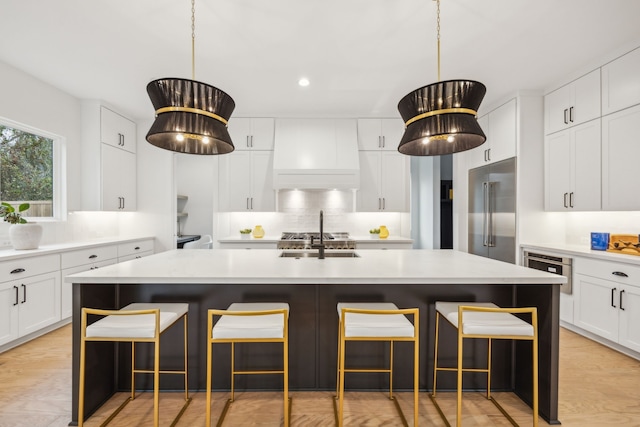 kitchen with white cabinets, stainless steel built in refrigerator, premium range hood, and a kitchen island with sink