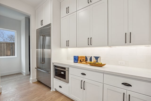 kitchen with white cabinetry, stainless steel appliances, light hardwood / wood-style floors, and backsplash