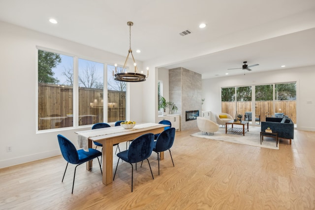 dining area featuring ceiling fan with notable chandelier, a fireplace, and light wood-type flooring