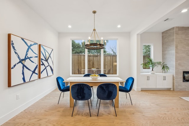 dining area featuring an inviting chandelier, a tiled fireplace, and light hardwood / wood-style flooring