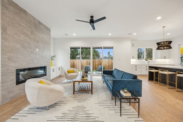 living room featuring ceiling fan, a healthy amount of sunlight, a tile fireplace, and light hardwood / wood-style flooring