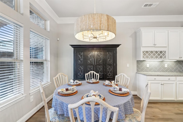 dining space with an inviting chandelier, ornamental molding, and light wood-type flooring