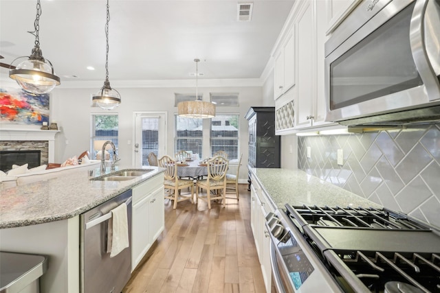 kitchen featuring appliances with stainless steel finishes, decorative light fixtures, sink, white cabinets, and a kitchen island with sink