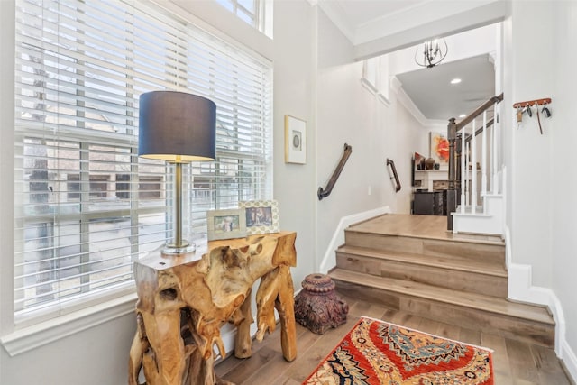 stairway featuring hardwood / wood-style flooring, a wealth of natural light, ornamental molding, and a chandelier