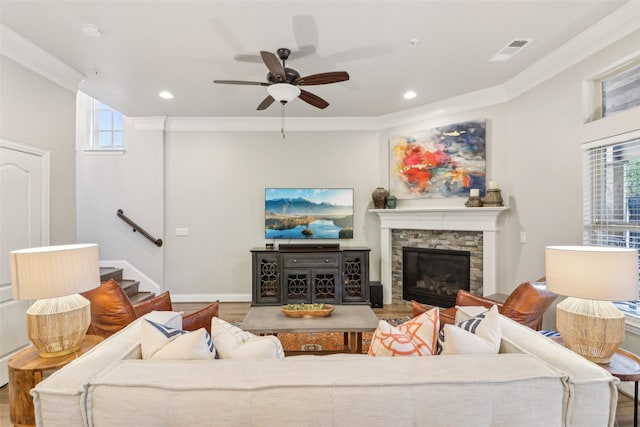 living room featuring crown molding, a stone fireplace, and plenty of natural light