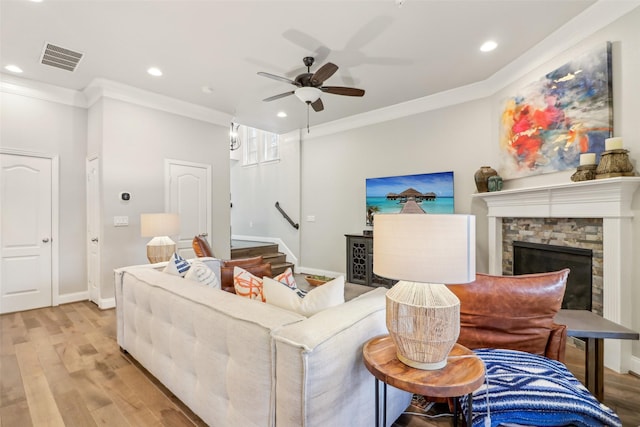 living room with crown molding, a fireplace, ceiling fan, and light wood-type flooring