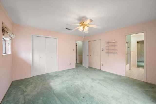 unfurnished bedroom featuring two closets, ensuite bath, light colored carpet, and ceiling fan