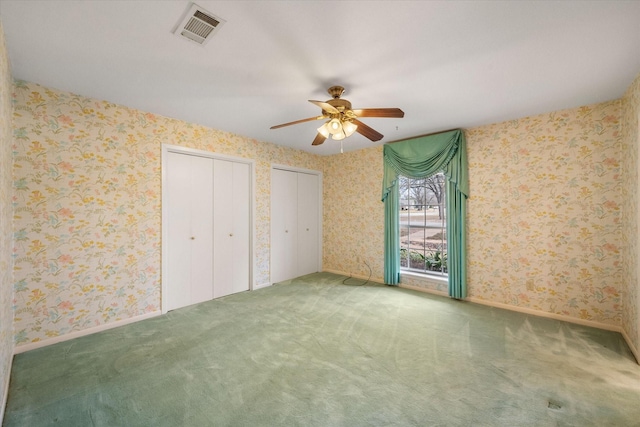 unfurnished bedroom with ceiling fan, multiple closets, and carpet