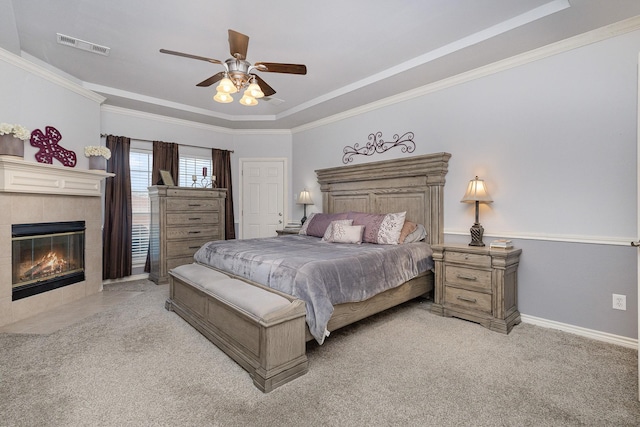 bedroom with a tray ceiling, crown molding, light colored carpet, and a tile fireplace