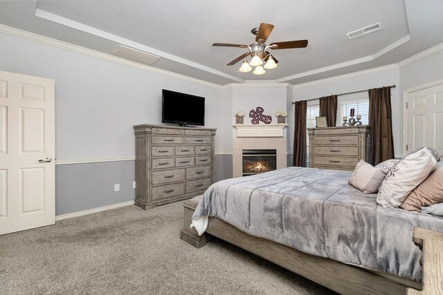 carpeted bedroom with a tiled fireplace, ornamental molding, a raised ceiling, and ceiling fan