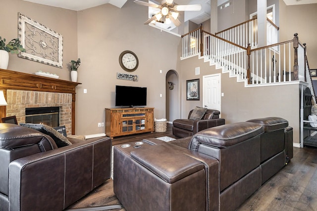 living room featuring dark hardwood / wood-style flooring, a towering ceiling, a fireplace, and ceiling fan