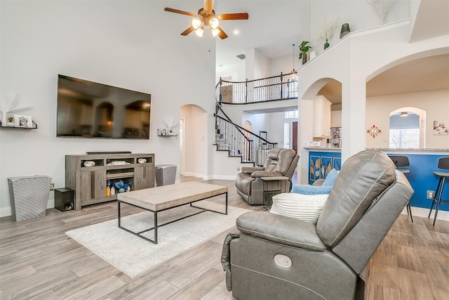 living room featuring ceiling fan, a towering ceiling, and light hardwood / wood-style floors