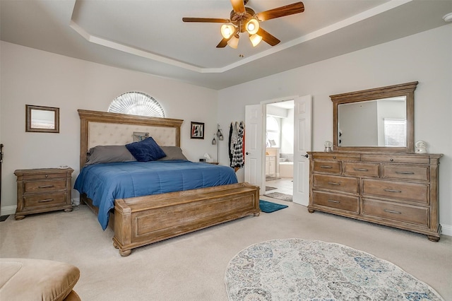 bedroom with a raised ceiling, ceiling fan, light carpet, and ensuite bath