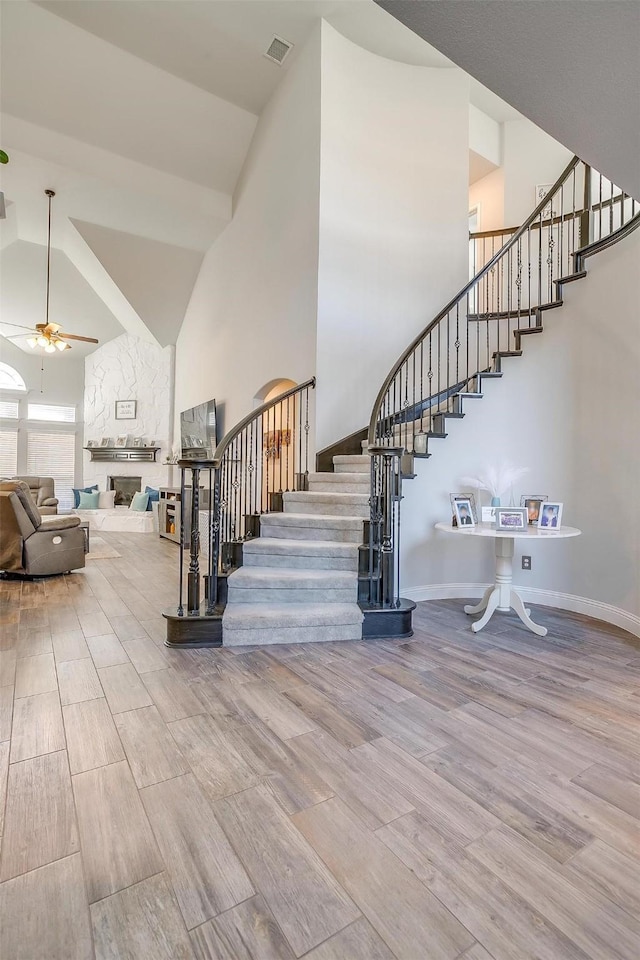 stairway featuring ceiling fan, high vaulted ceiling, hardwood / wood-style floors, and a fireplace