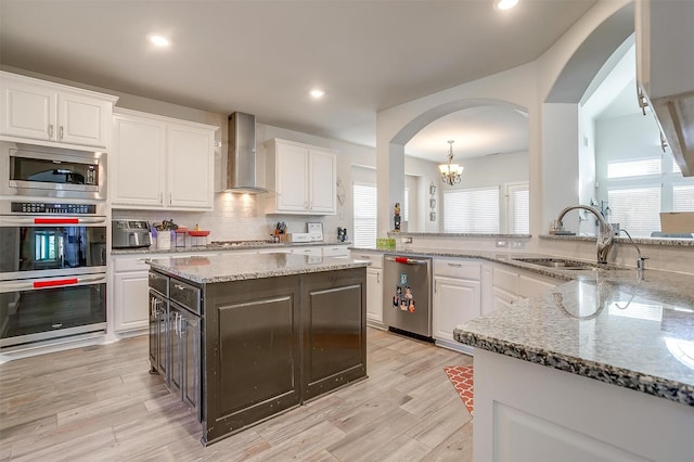 kitchen featuring white cabinetry, wall chimney exhaust hood, a center island, and sink