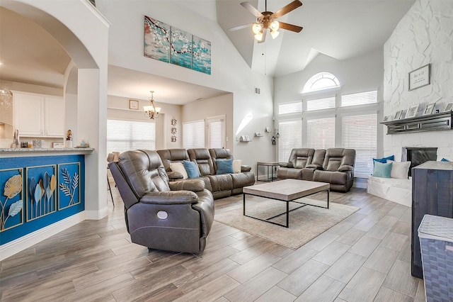 living room with a high ceiling, ceiling fan with notable chandelier, a wealth of natural light, and a fireplace