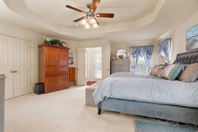 bedroom featuring light carpet, a tray ceiling, a closet, and ceiling fan