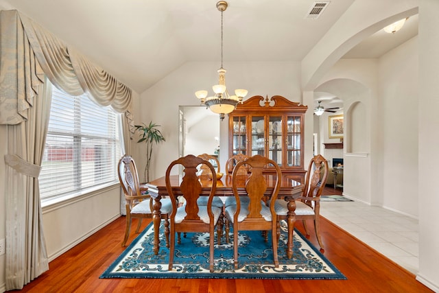 dining room with hardwood / wood-style floors, ceiling fan with notable chandelier, and vaulted ceiling