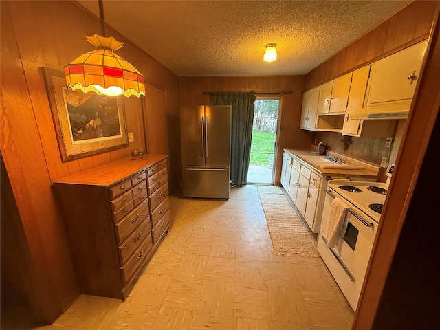 kitchen featuring wood walls, white electric stove, white cabinetry, stainless steel fridge, and hanging light fixtures