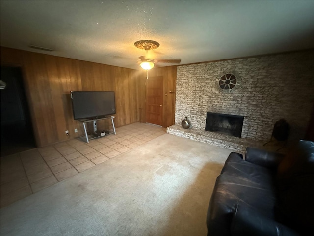 living room featuring light tile patterned flooring, wood walls, a textured ceiling, a brick fireplace, and ceiling fan