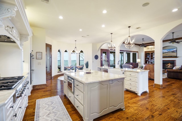 kitchen with hanging light fixtures, ceiling fan with notable chandelier, white cabinets, and a kitchen island