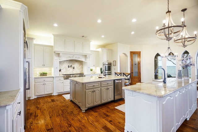 kitchen with white cabinetry, hanging light fixtures, light stone counters, stainless steel appliances, and a spacious island