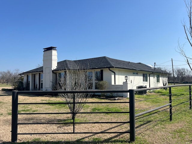 view of property exterior with roof with shingles, brick siding, a chimney, and cooling unit