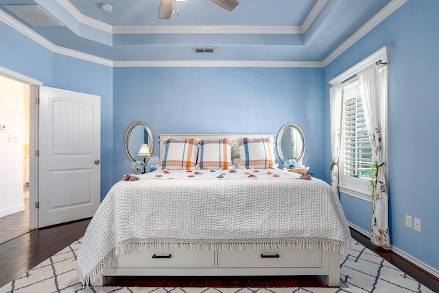 bedroom featuring dark hardwood / wood-style flooring, a tray ceiling, crown molding, and ceiling fan