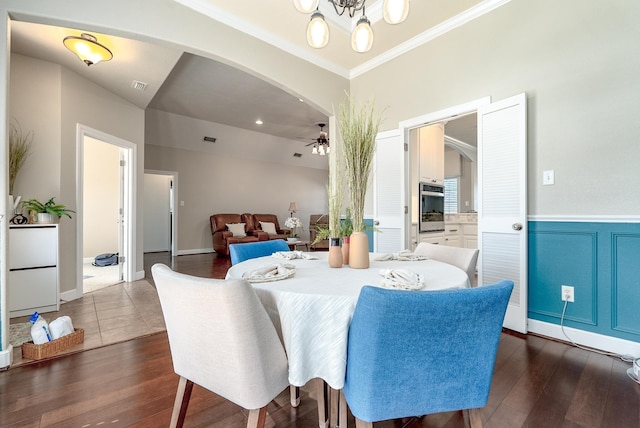 dining area with dark wood-type flooring, ornamental molding, and ceiling fan with notable chandelier