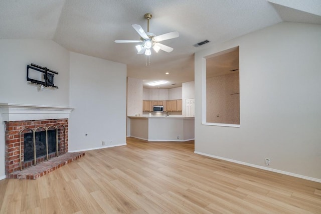 unfurnished living room featuring ceiling fan, vaulted ceiling, a brick fireplace, and light hardwood / wood-style flooring