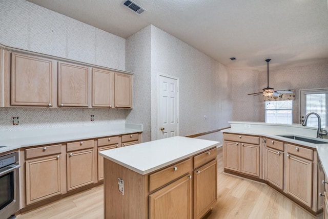 kitchen with sink, stainless steel oven, light hardwood / wood-style flooring, a kitchen island, and ceiling fan