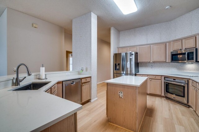 kitchen with a kitchen island, sink, stainless steel dishwasher, kitchen peninsula, and light hardwood / wood-style flooring