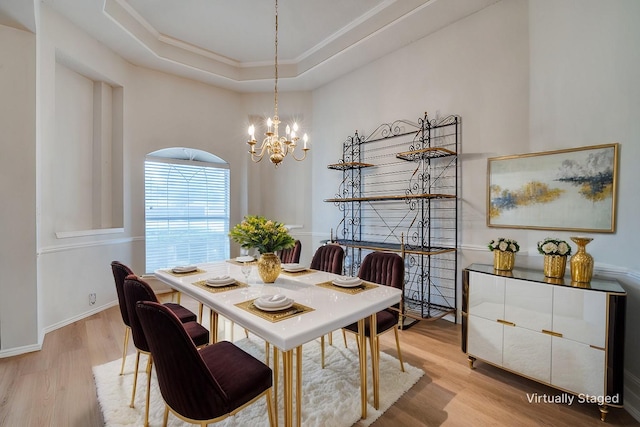 dining space with a raised ceiling, ornamental molding, an inviting chandelier, and light hardwood / wood-style floors