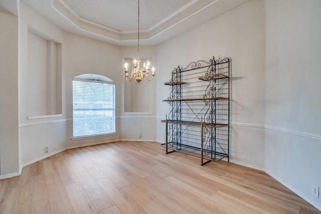 unfurnished dining area featuring a raised ceiling, ornamental molding, hardwood / wood-style flooring, and a chandelier