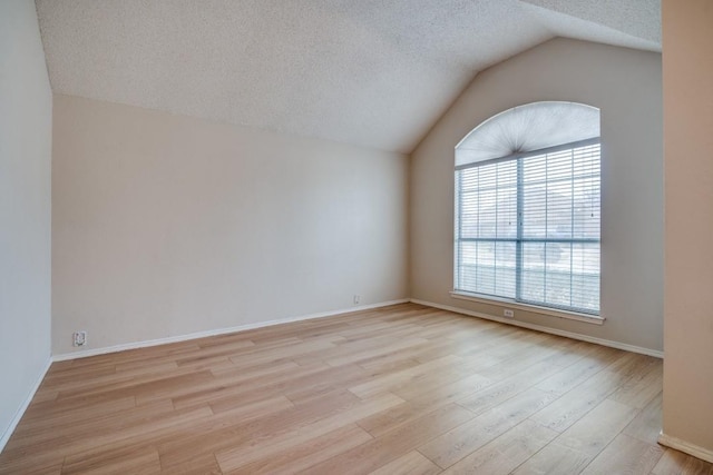 empty room featuring vaulted ceiling, light hardwood / wood-style floors, and a textured ceiling