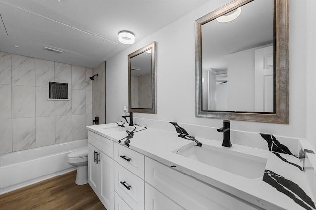 full bathroom with wood-type flooring, tiled shower / bath, vanity, and toilet