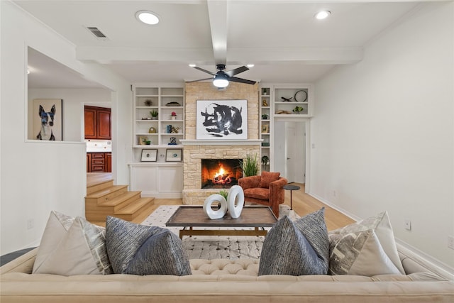 living room featuring ceiling fan, a stone fireplace, beamed ceiling, and light wood-type flooring