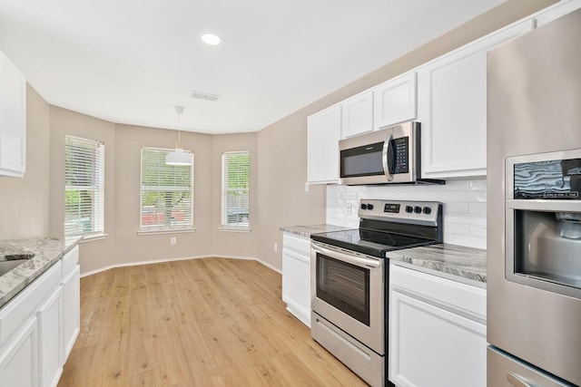 kitchen with pendant lighting, backsplash, white cabinets, light stone counters, and stainless steel appliances