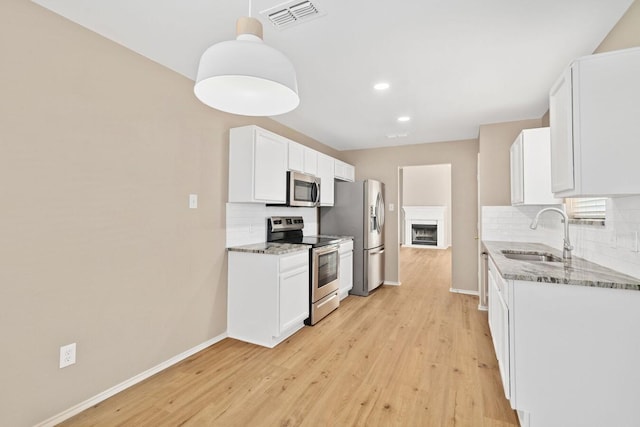 kitchen featuring sink, white cabinetry, hanging light fixtures, stainless steel appliances, and light stone countertops